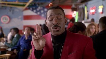 Movie still from “Boomerang” (1992), directed by Reginald Hudlin – A man in a red jacket holding up a peace sign with one hand; Close Up shot, High angle