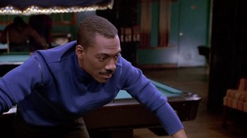 Movie still from “Boomerang” (1992), directed by Reginald Hudlin – A man in a blue shirt leaning over a pool table; Medium shot, Over the shoulder angle