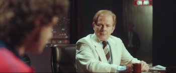 Movie still from “Borg vs. McEnroe” (2017), directed by Janus Metz – A man sitting in a chair wearing a suit and tie; Medium shot, Over the shoulder angle