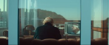 Movie still from “Borg vs. McEnroe” (2017), directed by Janus Metz – An older woman sitting on a couch watching television; Medium shot, Over the shoulder angle