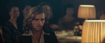 Movie still from “Borg vs. McEnroe” (2017), directed by Janus Metz – A man with long brown hair sitting in front of a group of people; Close Up shot, Over the shoulder angle