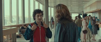 Movie still from “Borg vs. McEnroe” (2017), directed by Janus Metz – A man in a red and blue jacket is talking to a woman; Medium shot, Over the shoulder angle