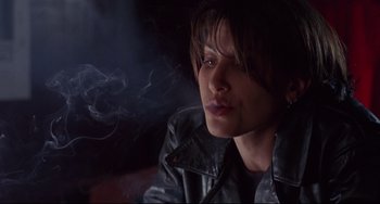 Movie still from “Bound” (1996), directed by Lilly Wachowski – A woman in a black leather jacket smoking a cigarette; Close Up shot, Over the shoulder angle