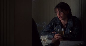 Movie still from “Bound” (1996), directed by Lilly Wachowski – A woman sitting at a table with a glass of beer in front of her; Medium shot, Over the shoulder angle