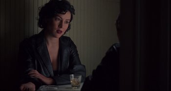 Movie still from “Bound” (1996), directed by Lilly Wachowski – A woman sitting at a table with a glass of whiskey; Medium shot, Over the shoulder angle
