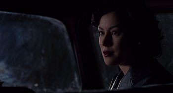 Movie still from “Bound” (1996), directed by Lilly Wachowski – A woman sitting in a car in the dark looking at the camera; Close Up shot, Over the shoulder angle