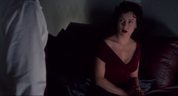 Movie still from “Bound” (1996), directed by Lilly Wachowski – A woman in a red dress sitting on a couch; Medium shot, Over the shoulder angle