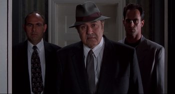 Movie still from “Bound” (1996), directed by Lilly Wachowski – A man in a suit and a hat standing in front of two other men; Medium shot, Low angle