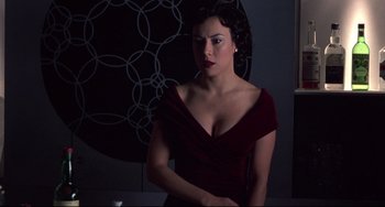 Movie still from “Bound” (1996), directed by Lilly Wachowski – A woman in a red dress is standing in a dark room; Medium shot, Over the shoulder angle