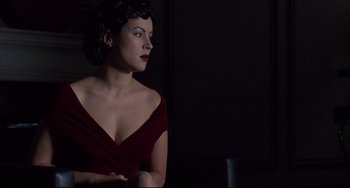 Movie still from “Bound” (1996), directed by Lilly Wachowski – A woman in a red dress is sitting in a dark room; Close Up shot, Low angle