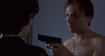 Movie still from “Bound” (1996), directed by Lilly Wachowski – A man holding a gun in front of another man; Close Up shot, Over the shoulder angle