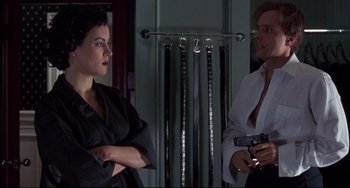 Movie still from “Bound” (1996), directed by Lilly Wachowski – A man and a woman standing next to each other holding a gun; Medium shot, Over the shoulder angle