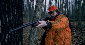 Movie still from “Bowling for Columbine” (2002), directed by Michael Moore – A man in an orange jacket is holding a rifle; Medium shot, Over the shoulder angle