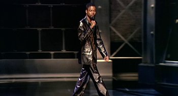 Movie still from “Bowling for Columbine” (2002), directed by Michael Moore – A man in a black and silver suit on a stage; Medium shot, High angle