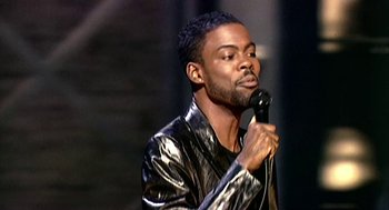 Movie still from “Bowling for Columbine” (2002), directed by Michael Moore – A man holding a microphone while wearing a leather jacket; Medium shot, High angle