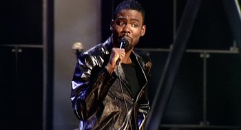 Movie still from “Bowling for Columbine” (2002), directed by Michael Moore – A man in a leather jacket is holding a microphone; Medium shot, High angle