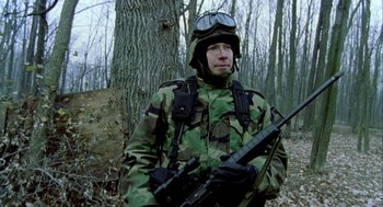 Movie still from “Bowling for Columbine” (2002), directed by Michael Moore – A man in camouflage holding a rifle in the woods; Medium shot, Low angle