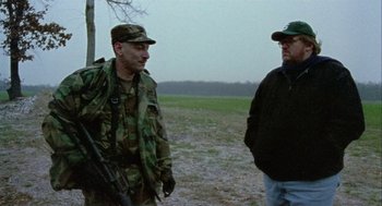 Movie still from “Bowling for Columbine” (2002), directed by Michael Moore – A man in a military uniform is standing next to another man in a field; Medium shot, Over the shoulder angle