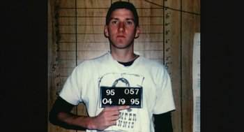 Movie still from “Bowling for Columbine” (2002), directed by Michael Moore – A man in a white t - shirt holding up a sign; Medium shot, Overhead angle