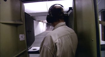 Movie still from “Bowling for Columbine” (2002), directed by Michael Moore – A man wearing a pair of ear muffs in a shooting range; Medium shot, High angle