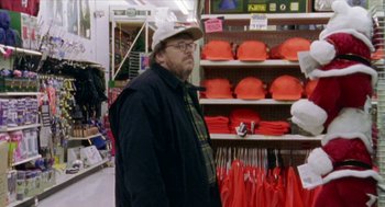 Movie still from “Bowling for Columbine” (2002), directed by Michael Moore – A man standing in front of a display of hats; Medium shot, Over the shoulder angle