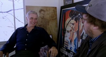 Movie still from “Bowling for Columbine” (2002), directed by Michael Moore – An older man standing in front of a painting; Medium shot, Over the shoulder angle