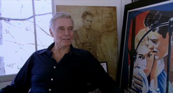 Movie still from “Bowling for Columbine” (2002), directed by Michael Moore – An older man standing in front of a painting; Medium shot, Over the shoulder angle