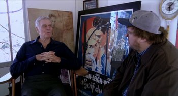 Movie still from “Bowling for Columbine” (2002), directed by Michael Moore – Two men sitting in front of a painting of a man and a woman; Medium shot, Over the shoulder angle