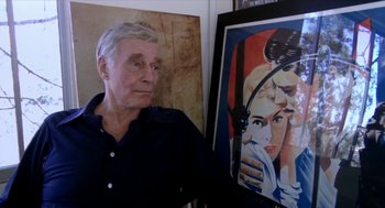 Movie still from “Bowling for Columbine” (2002), directed by Michael Moore – An older man standing in front of a painting; Close Up shot, Over the shoulder angle