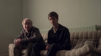 Movie still from “Boy A” (2007), directed by John Crowley – Two men sitting on a couch in front of a wall; Medium shot, Low angle