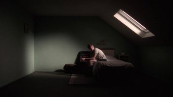 Movie still from “Boy A” (2007), directed by John Crowley – A man sitting on a bed in a room with the light on; Wide shot, Low angle