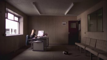 Movie still from “Boy A” (2007), directed by John Crowley – A woman sitting at a desk with a laptop computer; Wide shot, High angle