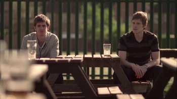 Movie still from “Boy A” (2007), directed by John Crowley – Two young men sitting at a picnic table with a glass of water in front of them; Medium shot, Over the shoulder angle