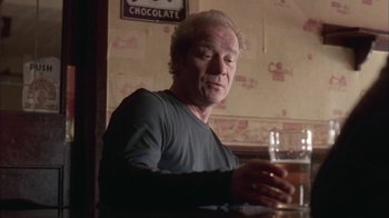 Movie still from “Boy A” (2007), directed by John Crowley – A man sitting at a table with a glass of beer; Medium shot, Low angle