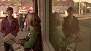 Movie still from “Boy A” (2007), directed by John Crowley – A woman standing in front of a building looking in a mirror; Medium shot, Over the shoulder angle