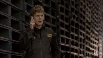 Movie still from “Boy A” (2007), directed by John Crowley – A man talking on a cell phone while standing in front of a wall; Medium shot, Low angle