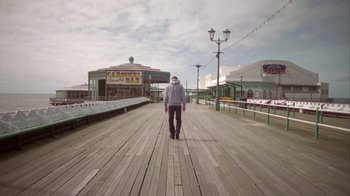 Movie still from “Boy A” (2007), directed by John Crowley – A person walking on a boardwalk near a pier; Wide shot, Low angle