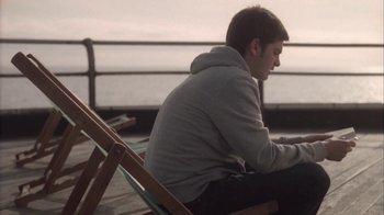 Movie still from “Boy A” (2007), directed by John Crowley – A man sitting in a chair on the beach; Medium shot, Low angle