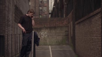 Movie still from “Boy A” (2007), directed by John Crowley – A man standing on a sidewalk next to an alley; Wide shot, Over the shoulder angle