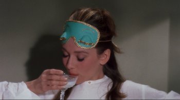 Movie still from “Breakfast at Tiffany's” (1961), directed by Blake Edwards – A woman wearing a mask drinking a glass of wine; Close Up shot, High angle