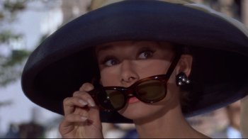 Movie still from “Breakfast at Tiffany's” (1961), directed by Blake Edwards – A person wearing sunglasses and a hat; Close Up shot, Over the shoulder angle