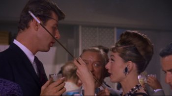 Movie still from “Breakfast at Tiffany's” (1961), directed by Blake Edwards – A man and a woman holding a straw to their face; Close Up shot, Over the shoulder angle