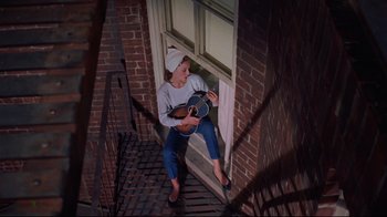 Movie still from “Breakfast at Tiffany's” (1961), directed by Blake Edwards – A woman sitting on a porch playing a guitar; Wide shot, Overhead angle