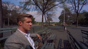 Movie still from “Breakfast at Tiffany's” (1961), directed by Blake Edwards – A man sitting on top of a wooden park bench; Wide shot, Over the shoulder angle