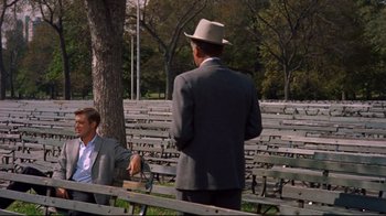 Movie still from “Breakfast at Tiffany's” (1961), directed by Blake Edwards – A man in a suit and a woman in a hat are sitting on a bench; Wide shot, Over the shoulder angle
