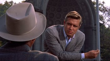 Movie still from “Breakfast at Tiffany's” (1961), directed by Blake Edwards – A man wearing a suit and a hat is talking to another man in front of a building; Medium shot, Over the shoulder angle