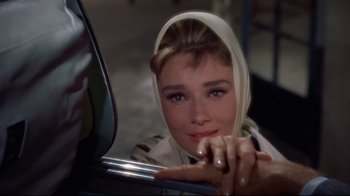 Movie still from “Breakfast at Tiffany's” (1961), directed by Blake Edwards – A person wearing a headscarf in a parking lot; Close Up shot, Over the shoulder angle