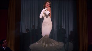 Movie still from “Breakfast at Tiffany's” (1961), directed by Blake Edwards – A woman in a white dress and white gloves on a stage; Medium shot, Low angle