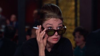 Movie still from “Breakfast at Tiffany's” (1961), directed by Blake Edwards – A woman with sunglasses and a cigarette in her mouth; Close Up shot, Over the shoulder angle