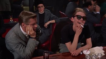 Movie still from “Breakfast at Tiffany's” (1961), directed by Blake Edwards – A man sitting next to another man while smoking a cigarette; Medium shot, Over the shoulder angle